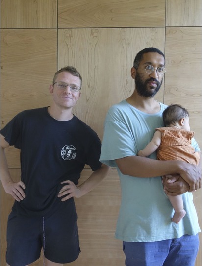 Alex and James standing together in the workshop, James holding his baby