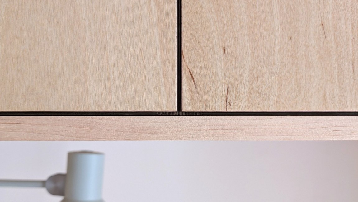 Close-up of the joint between two plywood panels, showing the narrow shadow gap and the layered plywood edge