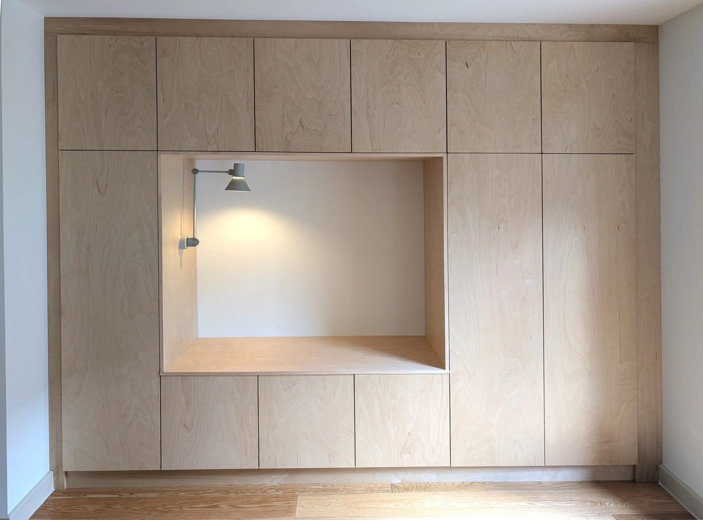 Full-height plywood joinery wall, straight on, with the lit seating nook set into the centre