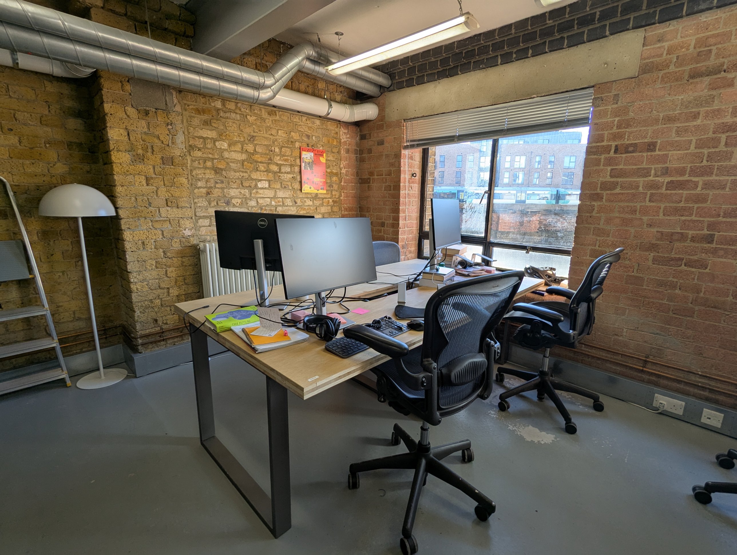 Desk in solid-core door blank over steel legs, with two monitors, against an exposed brick wall