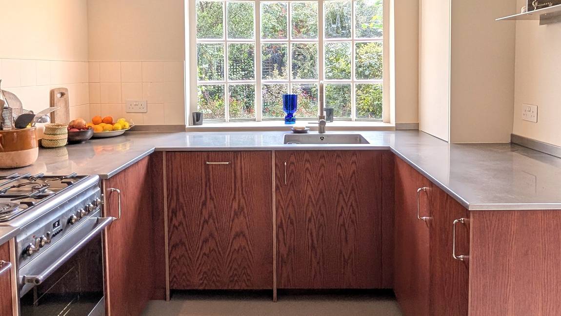 Oak-veneered plywood kitchen cabinets dyed a red mahogany, with a stainless steel worktop and welded sink