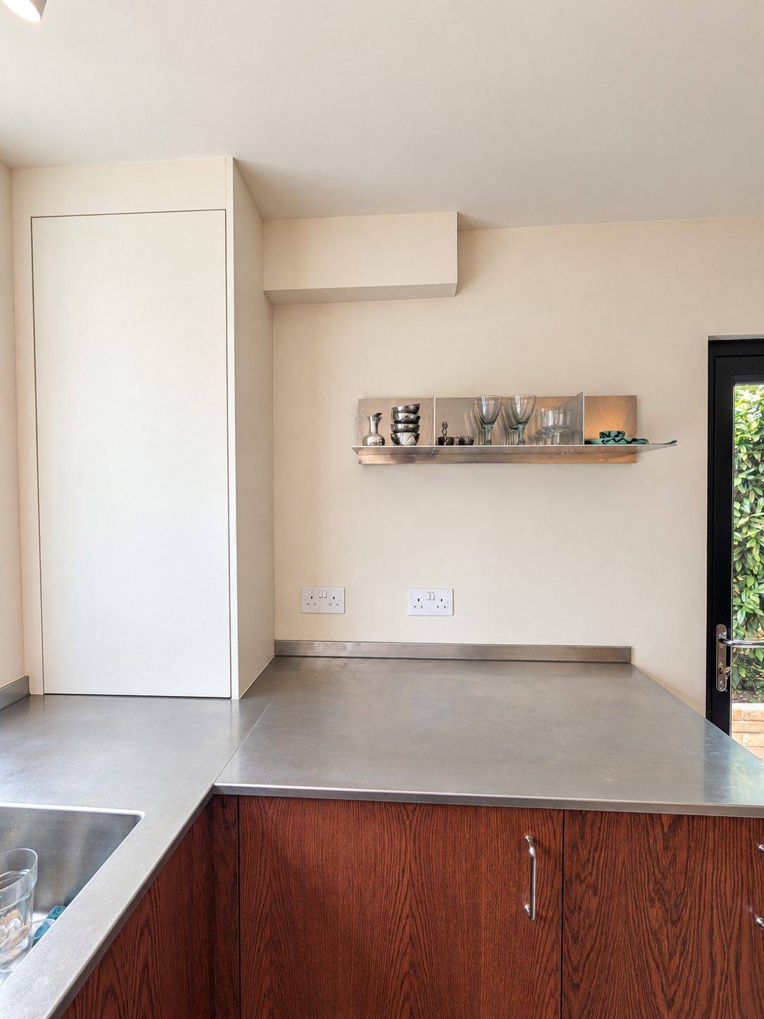 The neutral boiler cupboard and stainless shelf, rebuilt to read as the wall rather than as cabinetry