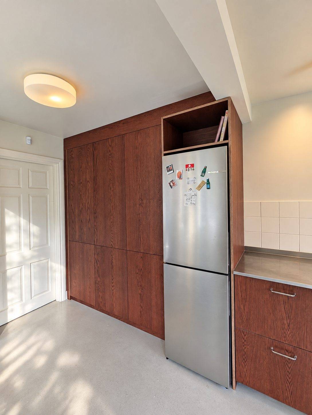 The custom fridge housing beside the tall run of oak-veneered cabinets