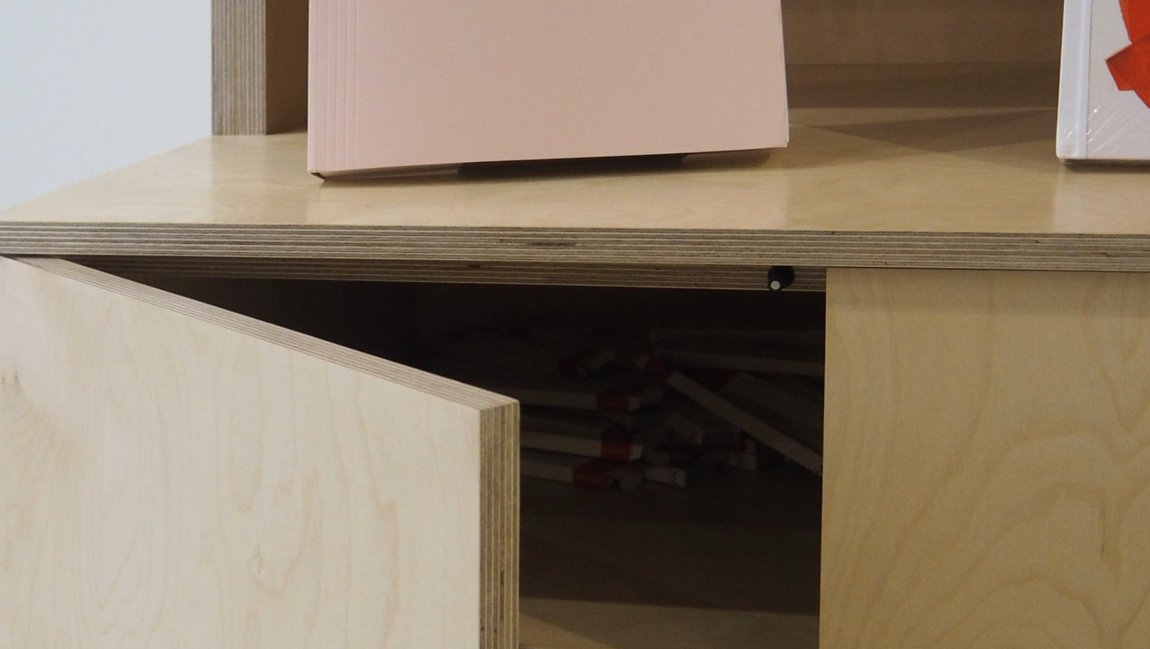 Detail of the open cabinet below the reception desk, showing the plywood edge